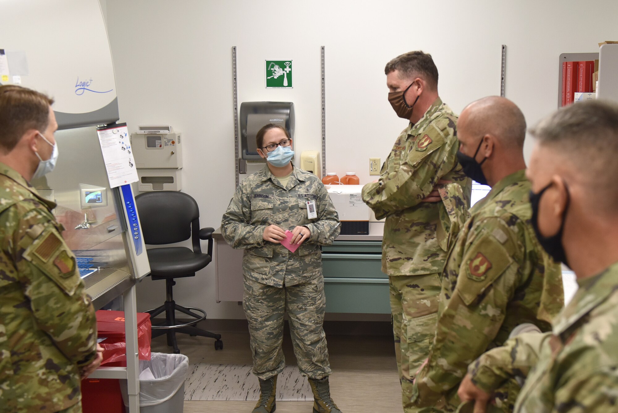 Photo shows an individual standing in front of lab testing equipment while explaining its use to a group of individuals.