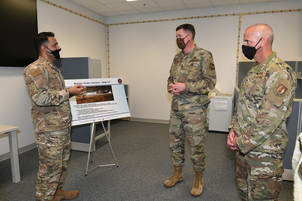 Photo shows three individual standing and speaking to each other in front of an easel.