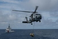 A U.S. Navy helicopter transfer suspected contraband from a U.S. Coast Guard Cutter.