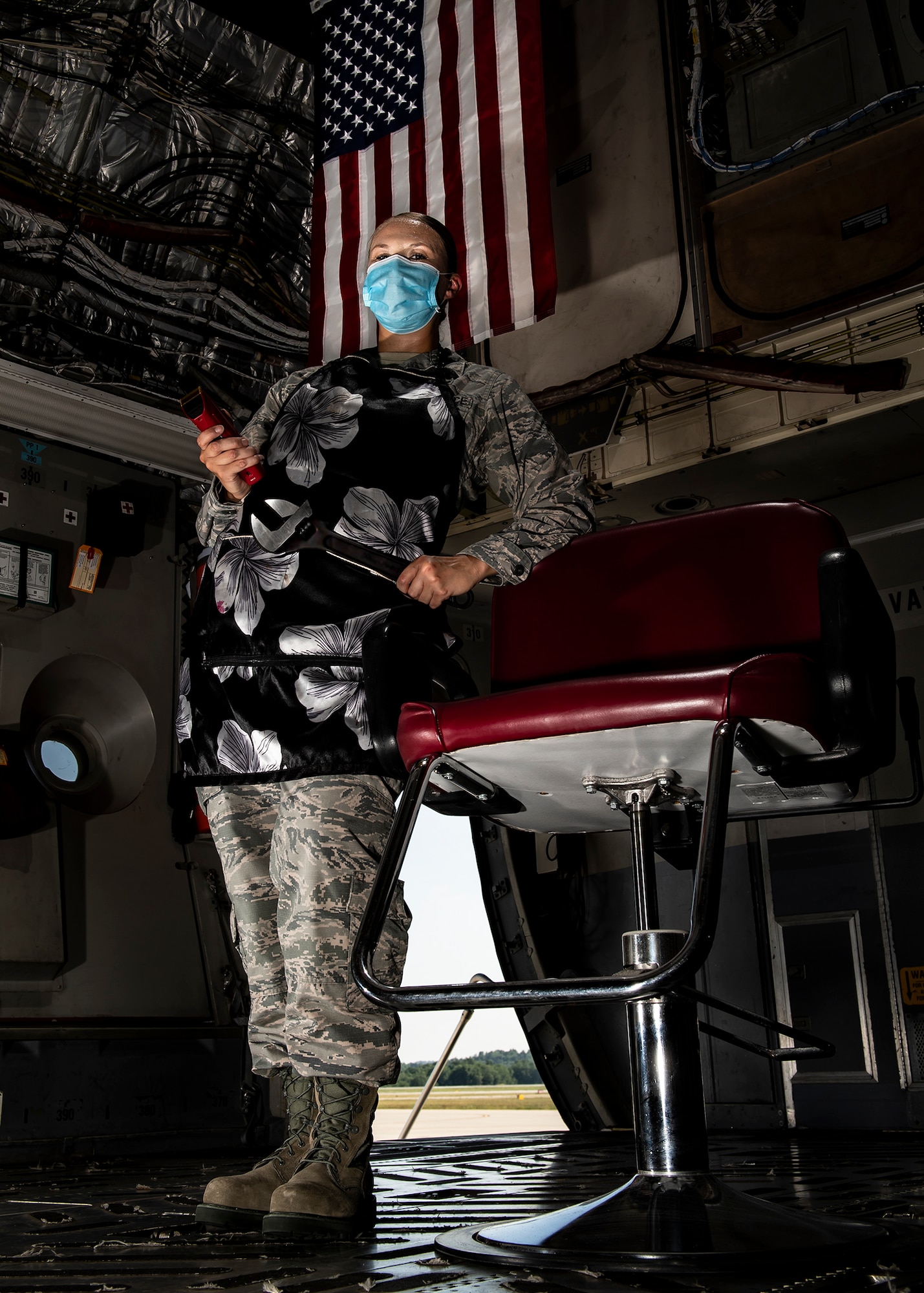Senior Airman Sara Gutherie, 911th Aircraft Maintenance Squadron integrated flight control systems mechanic, poses for a photo inside a C-17 Globemaster III with a wrench and hair clippers while wearing an apron and personal protective equipment at the Pittsburgh International Airport Air Reserve Station, Pennsylvania, July 8, 2020. During COVID-19 restrictions, Gutherie helped her fellow Airmen by using her skills as a licensed cosmetologist to give them haircuts to ensure they stayed within regulations while taking donations for the Needy Airman Fund in return. (U.S. Air Force photo by Joshua J. Seybert)