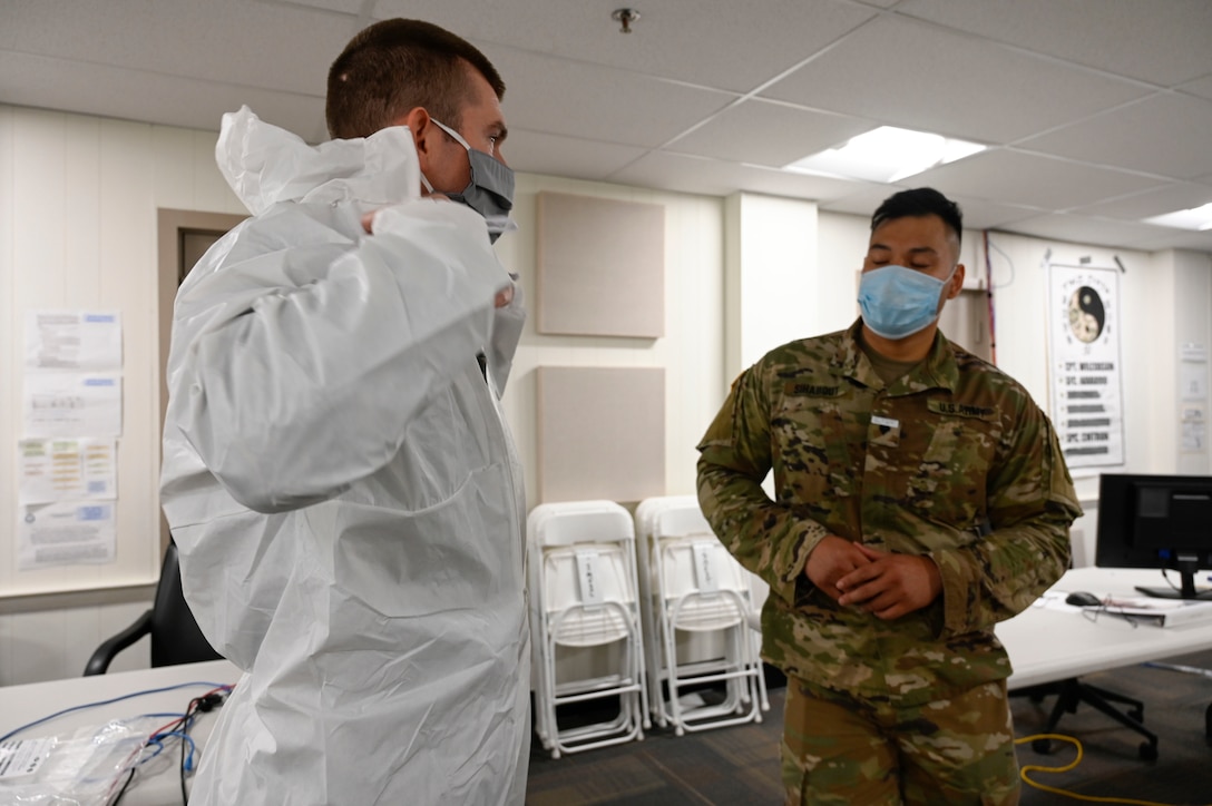 An airman demonstrates how to put on a Tyvek suit.