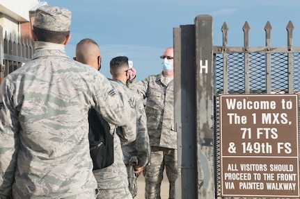 Airmen line up at a gate opening waiting to have their temperature checked