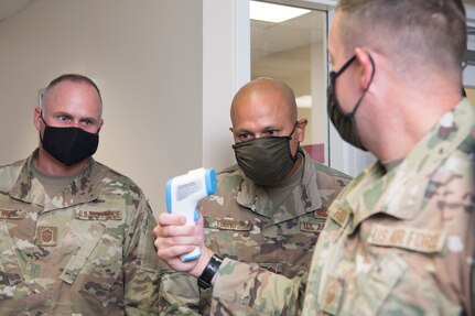 An Airman holds up a thermometer to show two others the reading