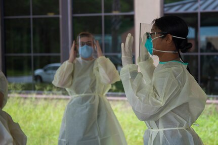 Hospital Corpsman Petty Officer 1st Class Shamace Phillips, a preventative medicine technician assigned to the Navy Medicine Readiness and Training Command, demonstrates the correct way to wear the personal protective equipment that is used to test patients for COVID-19 on July 8, 2020, at the Naval Health Clinic Charleston on Joint Base Charleston, S.C. Hospital Corpsmen from the NHCC were tasked with learning how to administer a COVID-19 swab test. The training will be used to test symptomatic patients and Sailors, as well as asymptomatic Sailors to attempt to lessen the spread of the virus.