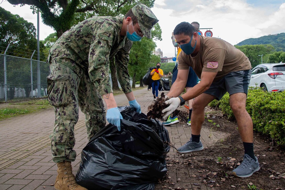 Two sailors put leaves and dirt in a trash bag.