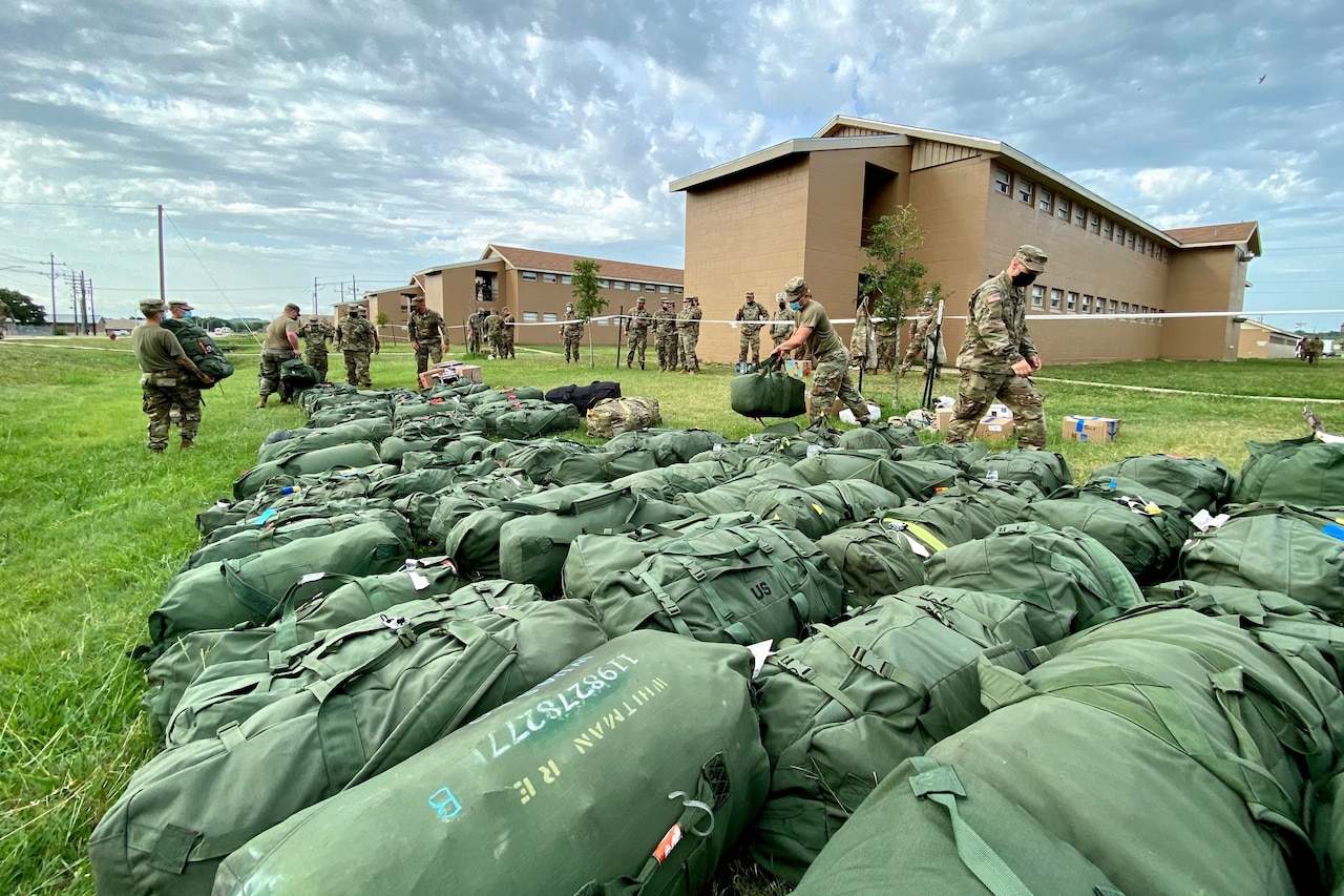 Soldiers line up dozens of stuff duffel bags after unloading them from a truck.