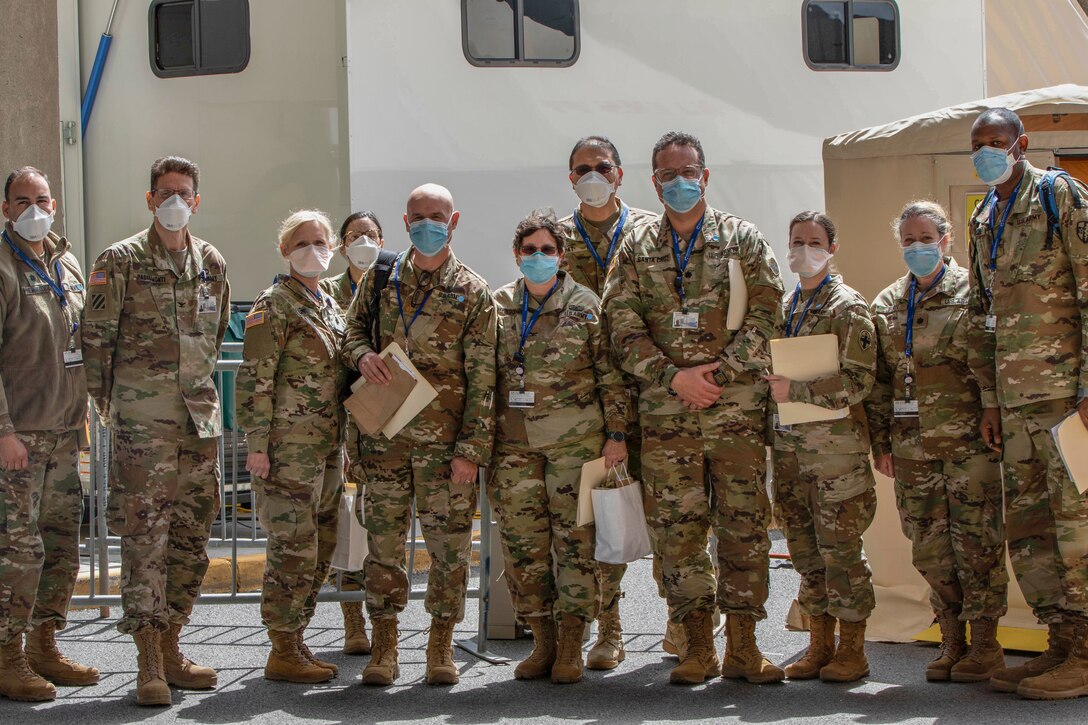 Members of a military medical task force wearing face masks and camouflage uniforms pose for a group photo. Some hold file folders.