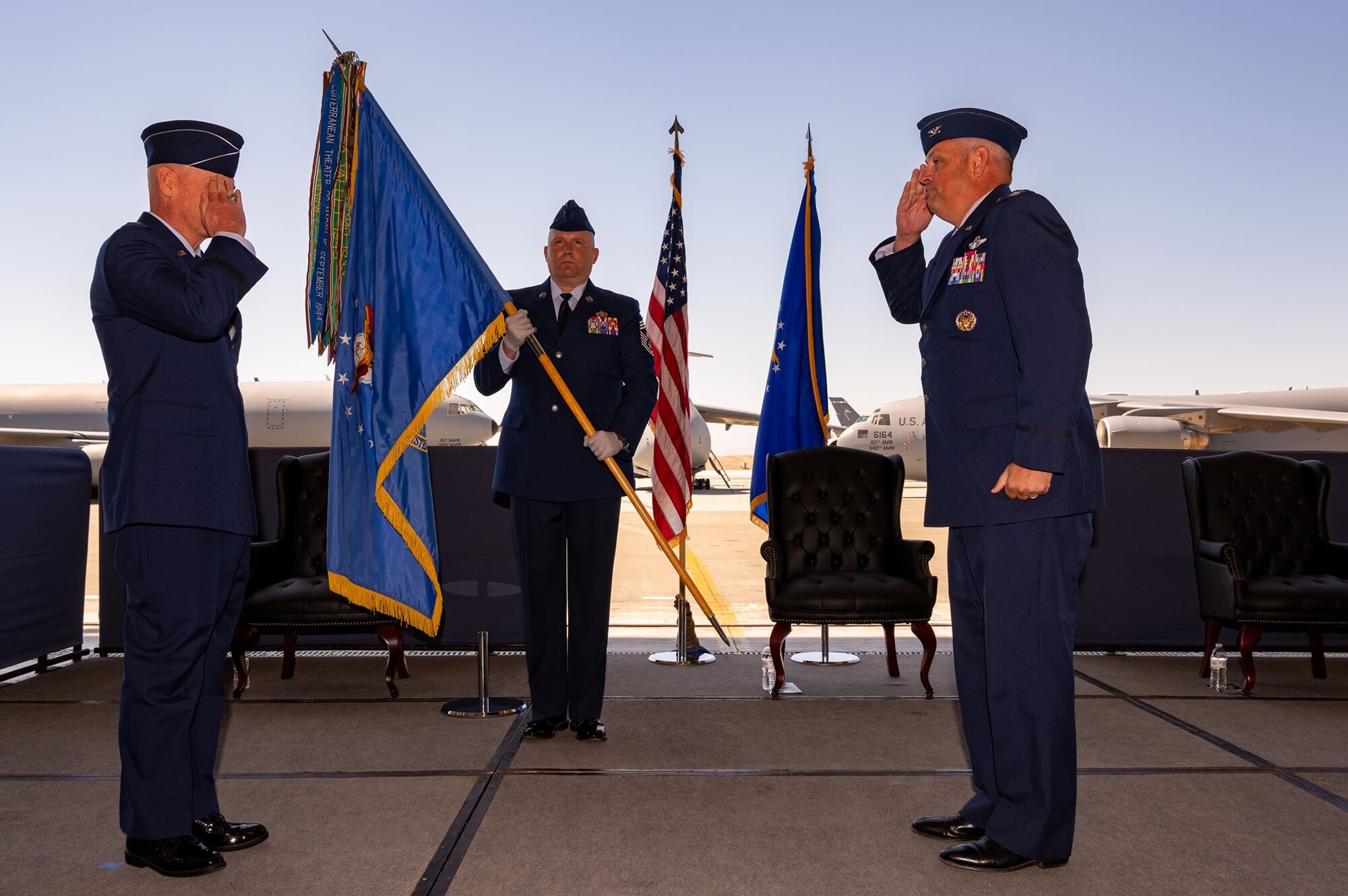 Two men in dress uniform salute each other while a third stands in the background and holds a guidon