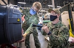 Gunner's Mate 1st Class Joshua Heitmann, right, a SurgeMain Sailor, practices installing a drum cover on a Close-In Weapons System mock-up with Fire Controlman 1st Clastt Kevin Flynn in the Shop 38 Gun Shop, July 15, 2020 at Puget Sound Naval Shipyard & Intermediate Maintenance Facility Detachment Everett.