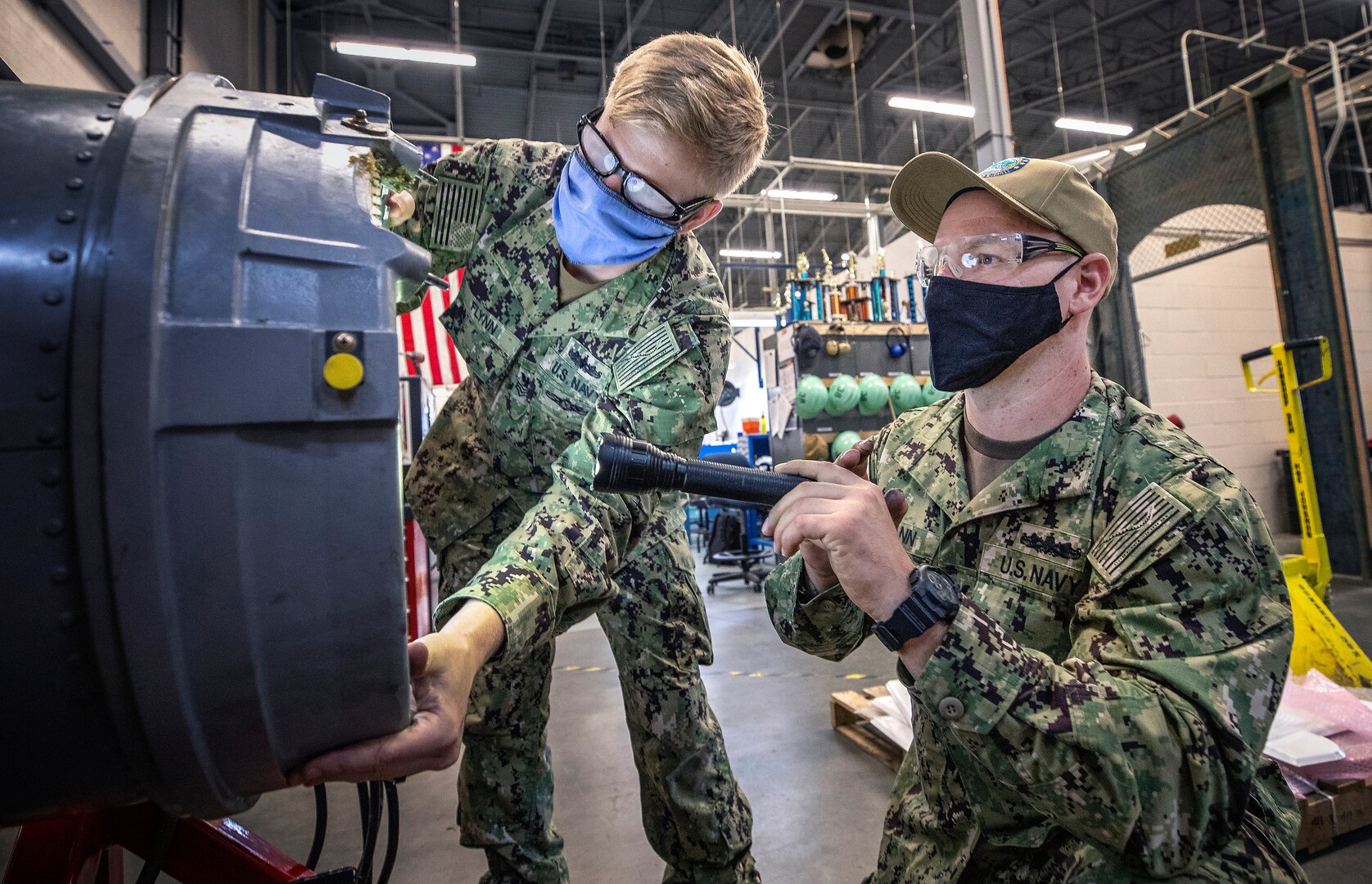 Gunner's Mate 1st Class Joshua Heitmann, right, a SurgeMain Sailor, practices installing a drum cover on a Close-In Weapons System mock-up with Fire Controlman 1st Clastt Kevin Flynn in the Shop 38 Gun Shop, July 15, 2020 at Puget Sound Naval Shipyard & Intermediate Maintenance Facility Detachment Everett.
