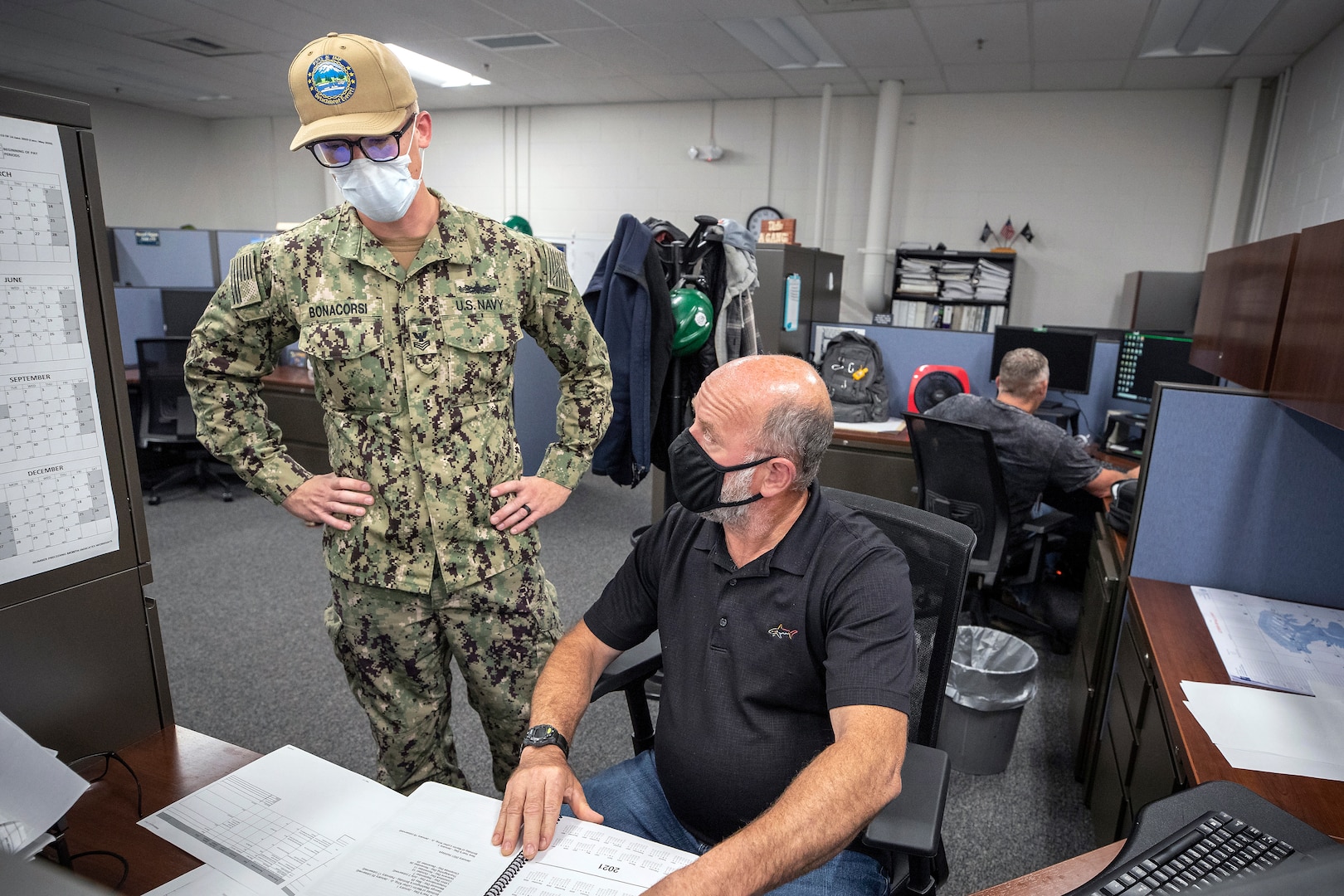 Electrician's Mate 1st Class Cory Bonacorsi, left, a newly-arrived Surge Main Sailor, talks with Steven Hall, Code 210.3 engineer, July 15, 2020 in the office at Puget Sound Naval Shipyard & Intermediate Maintenance Facility Detachment Everett.