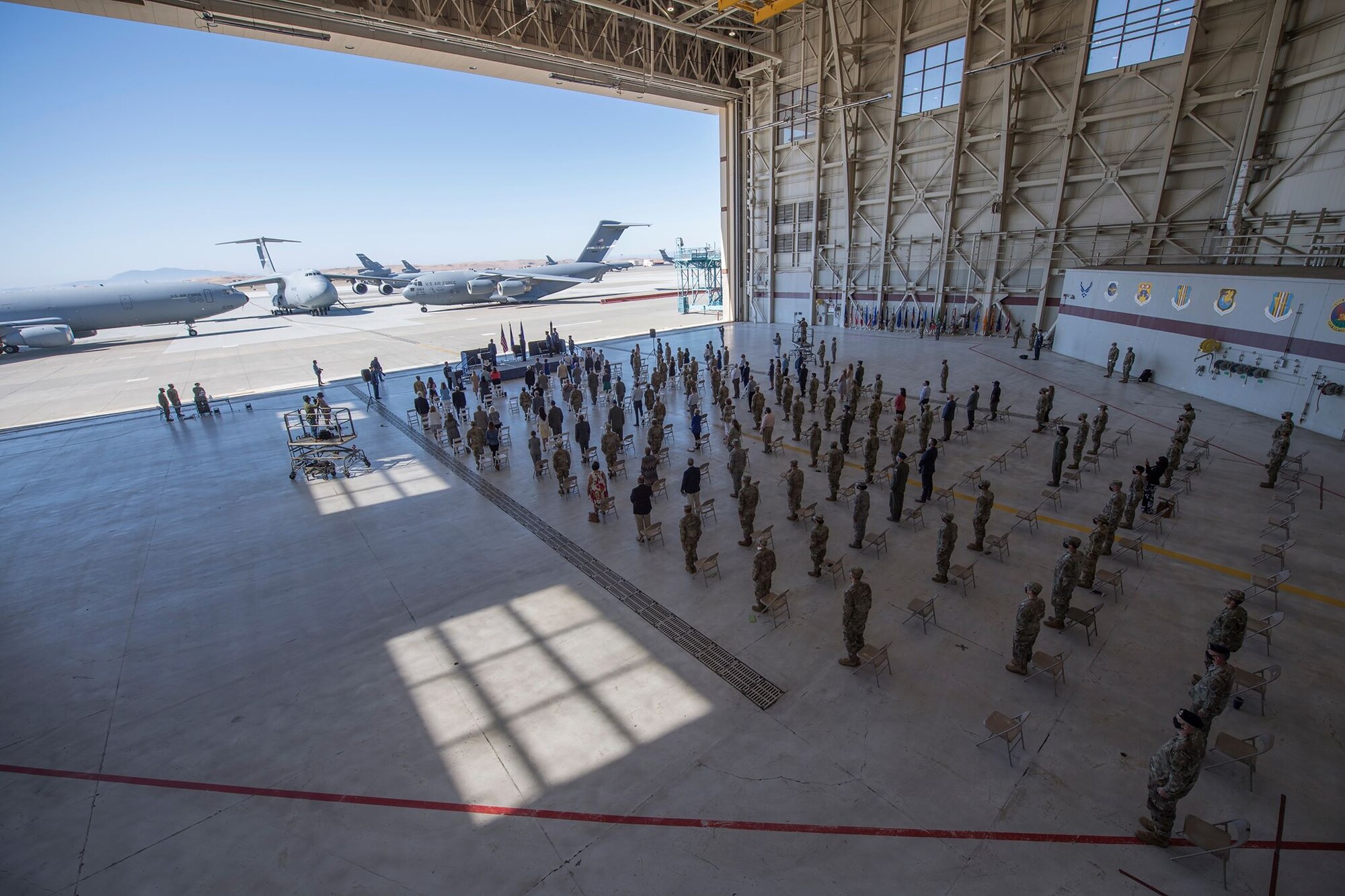 People stand in formation facing a stage inside of an aircraft hangar