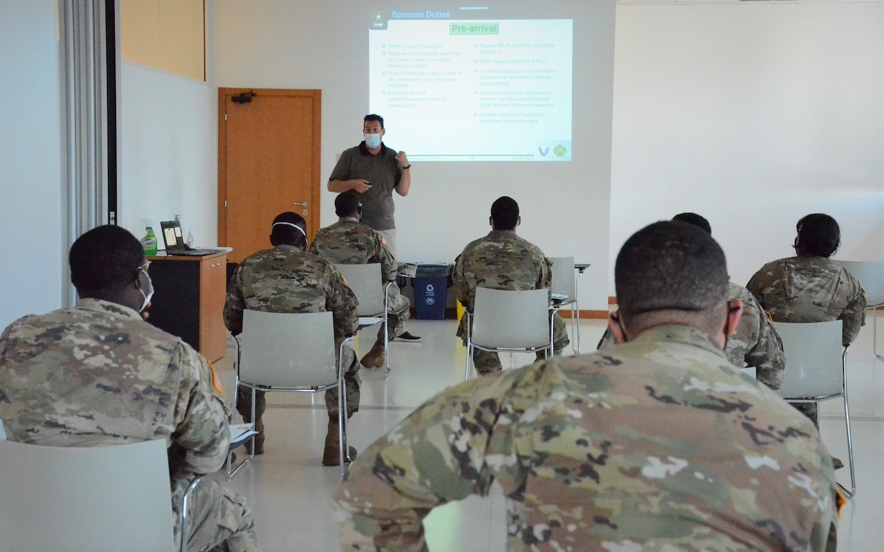 A man wearing a face mask presents a briefing to masked soldiers who are seated in a classroom.