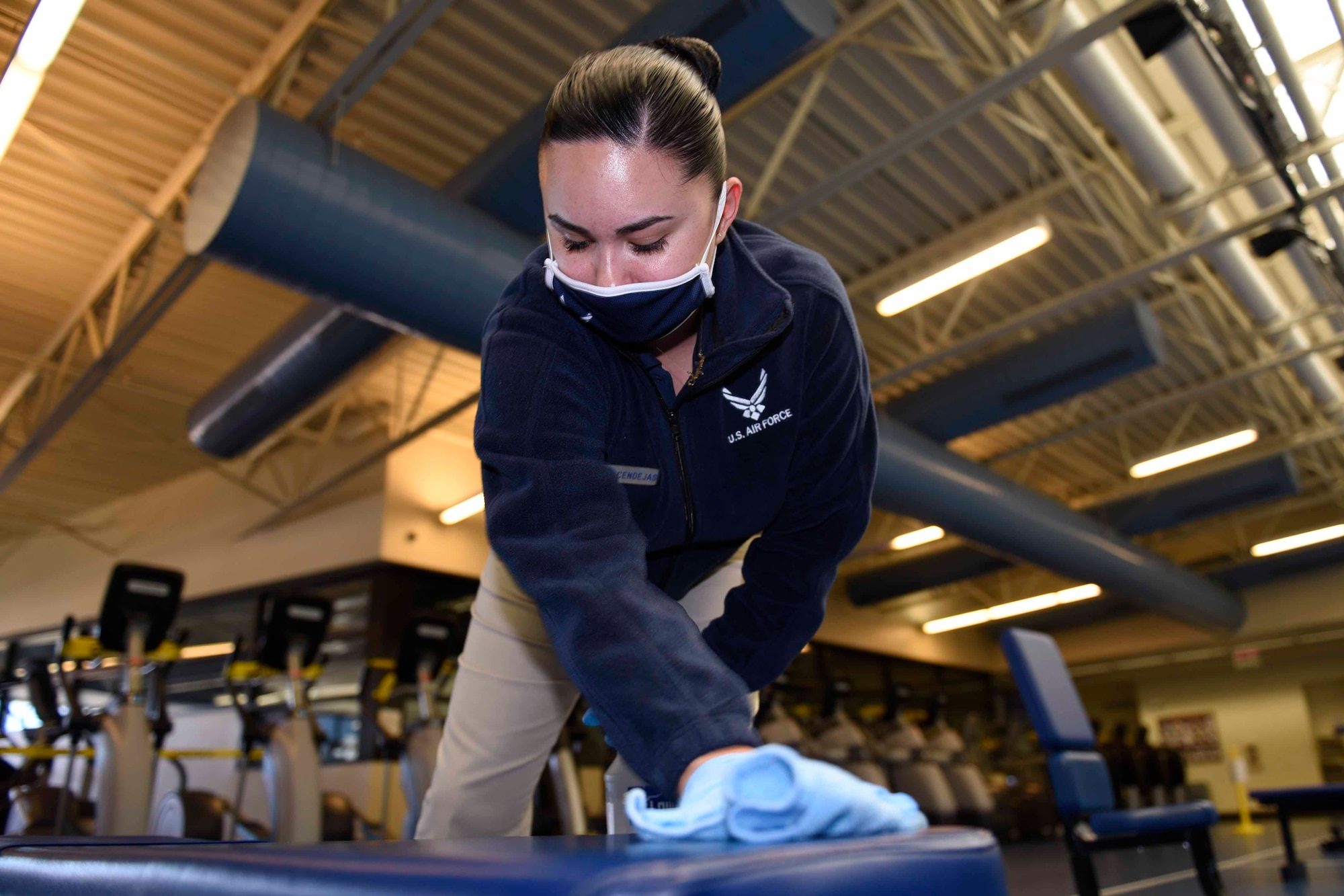 U.S. Air Force Senior Airman Angelina Cendejas, 60th Force Support Squadron fitness specialist, wipes down a bench June 24, 2020, at Travis Air Force Base, California. Fitness center staff members at Travis AFB sanitize equipment every hour to prevent the spread of COVID-19. (U.S. Air Force photo by Airman 1st Class Cameron Otte)