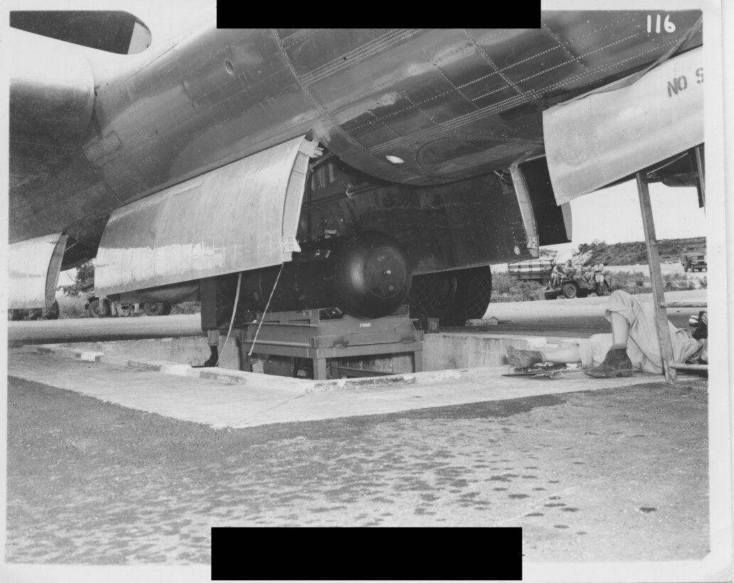 A bomb sits on the loading bay under the underbelly of a plane.