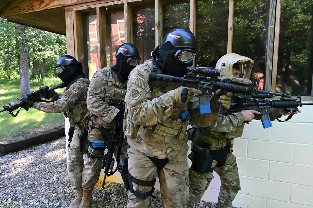 Four military members wear personal protective equipment as they prepare to enter a training structure while conducting military training at Camp Gilbert C. Grafton, near Devils Lake, N.D., July 16, 2020. They are carrying M4 rifles set up to fire simunition training rounds, similar to paintball, for realistic training.