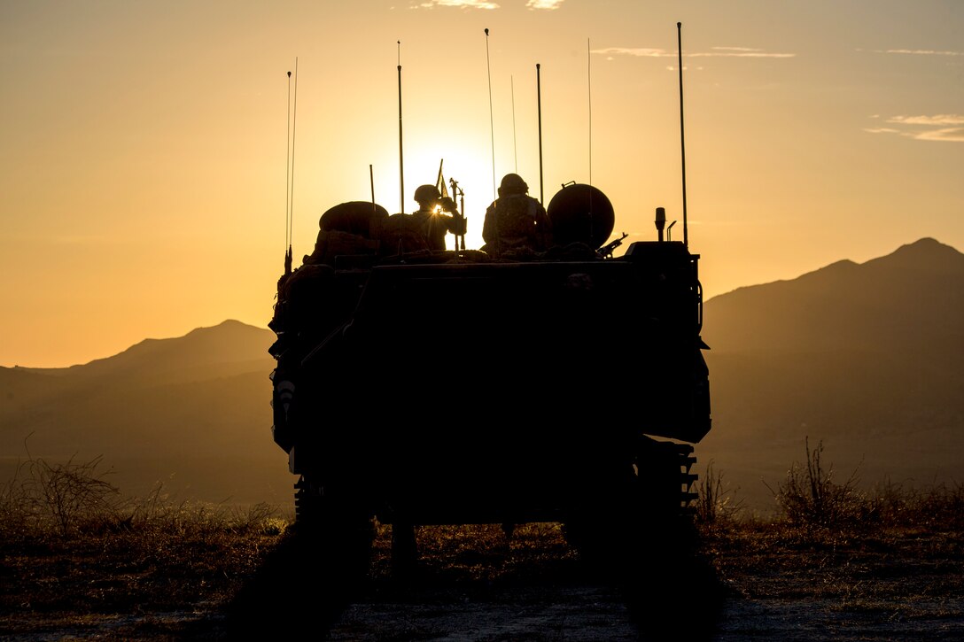 Marines are perched atop an amphibious assault vehicle, shown in silhouette, with mountains and an orange sky as the backdrop.
