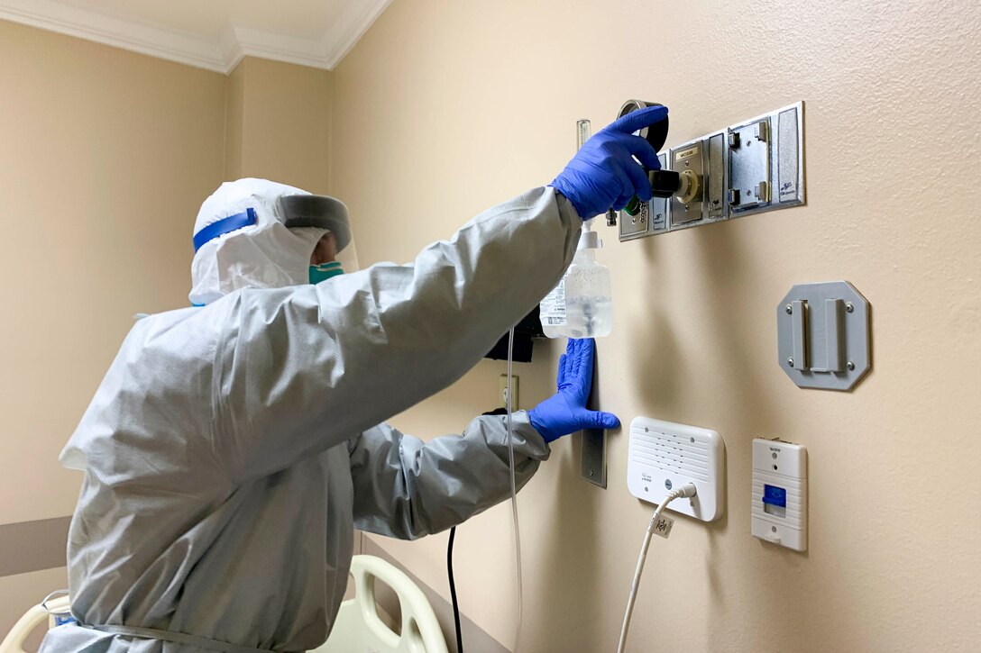 A soldier wearing personal protective equipment installs a piece of equipment on a wall.