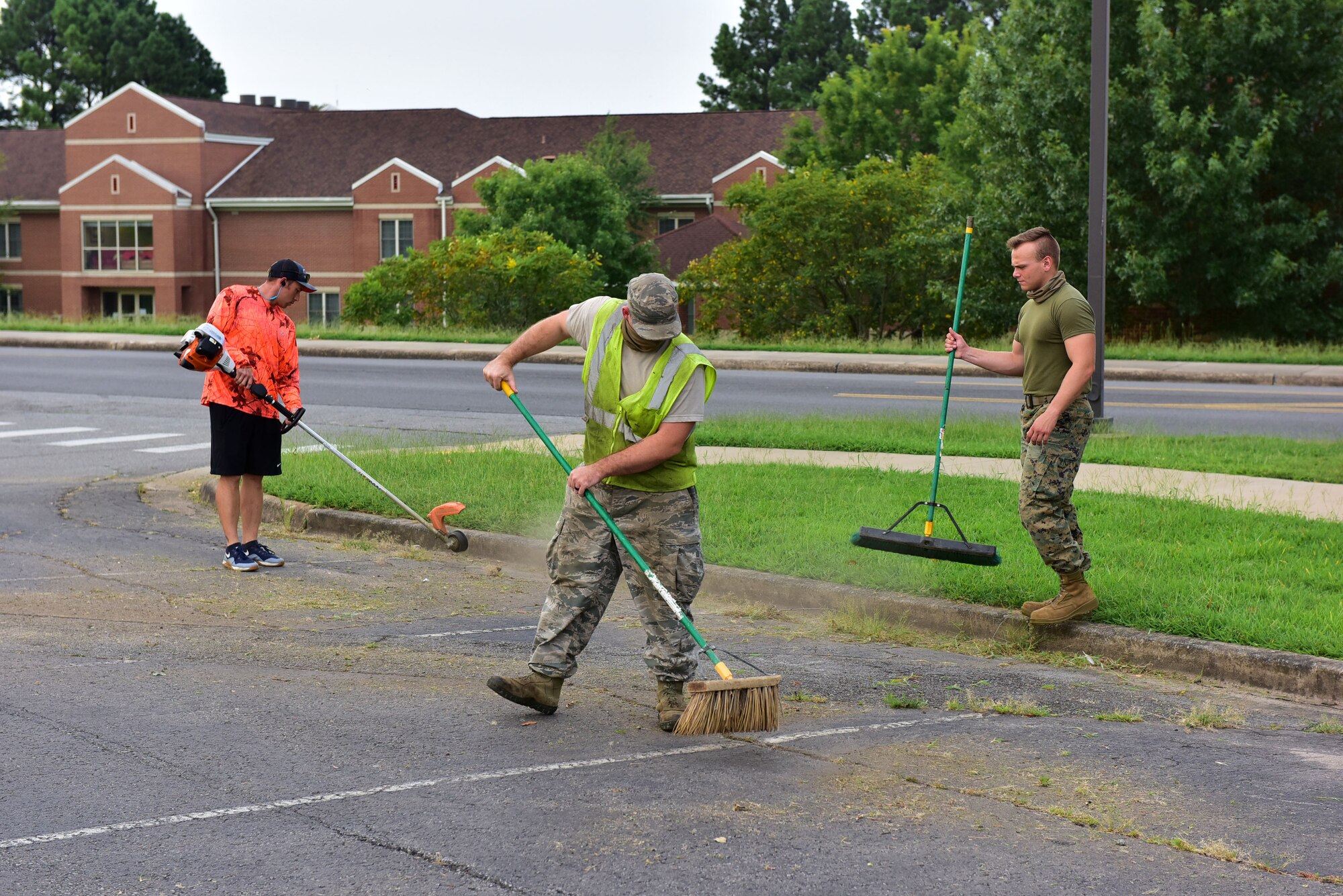 Multiple Airman sweeping grass up from sidewalks and parking lot