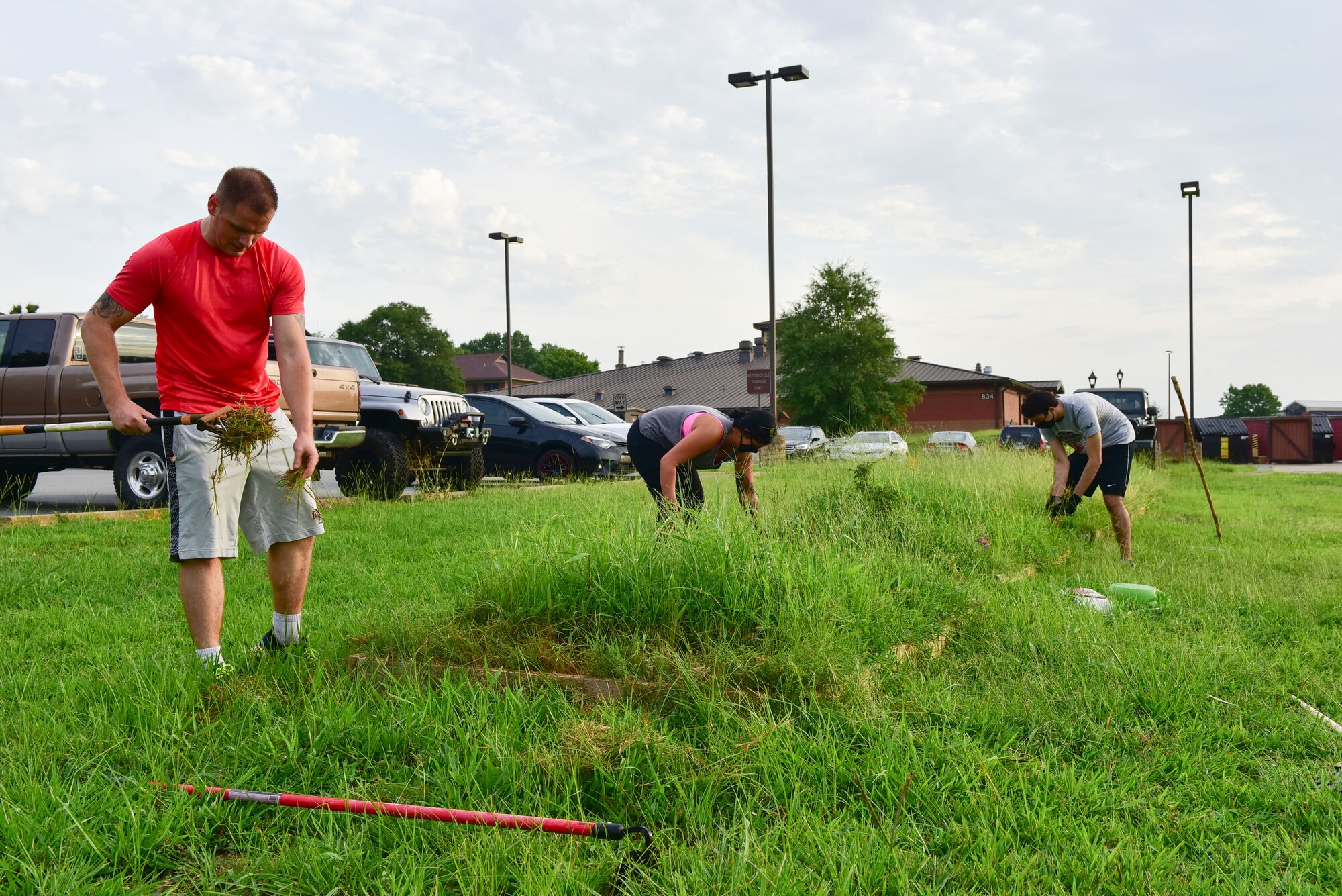 Airmen cutting grass and removing weeds from flowerbed