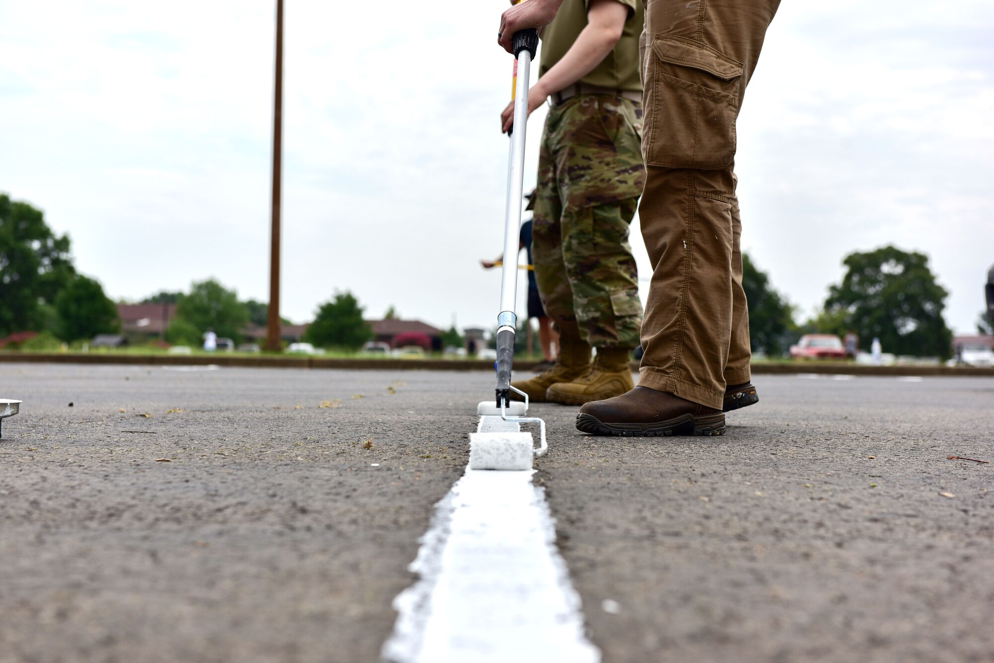 Airman with paintbrushes paint white lines in parking lots