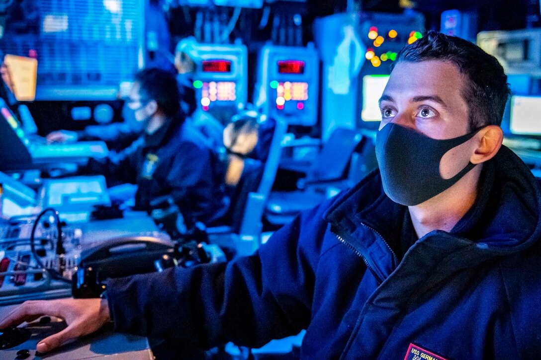 A sailor wearing a mask sits at a console in a blue-lit room.