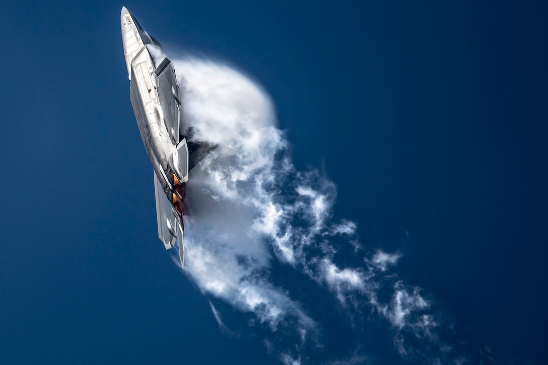 An Air Force jet creates a dramatic cloud burst as it turns in a blue sky.