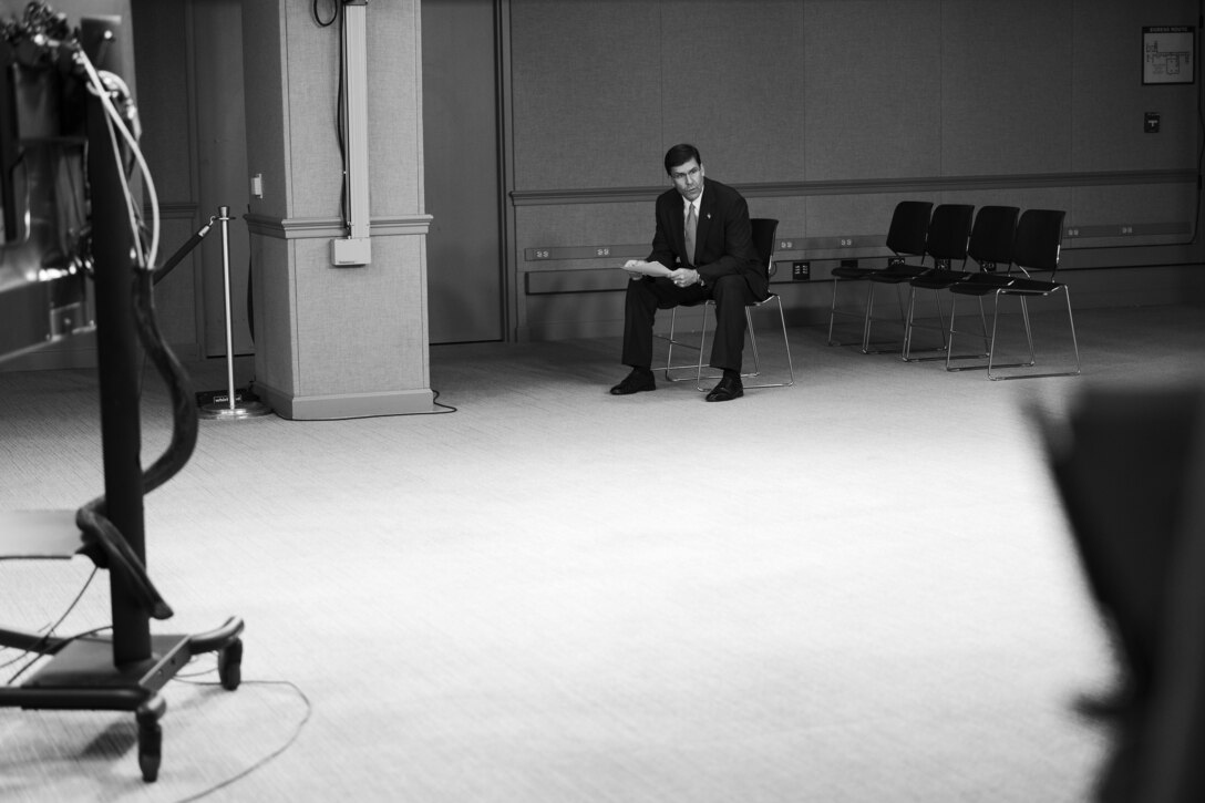 Black-and-white photo of a man sitting in a chair in a studio.