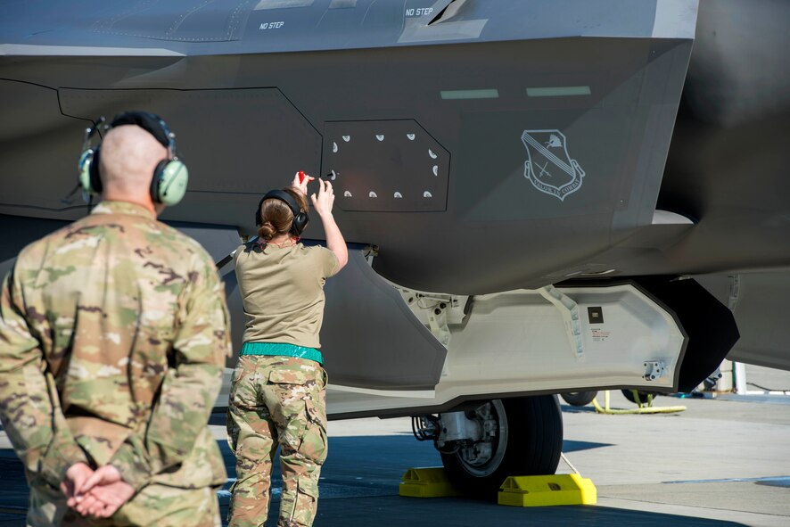 Airman 1st Class Lukas Turley, 354th Aircraft Maintenance Squadron crew chief, watches as Airman 1st Class Kelly McKamy, a 354th Aircraft Maintenance Squadron weapons load crew member, both assigned to Eielson Air Force Base, Alaska, closes the maintenance interface panel on an F-35 Lightning II at Joint Base Elmendorf-Richardson, Alaska, July 14, 2020.