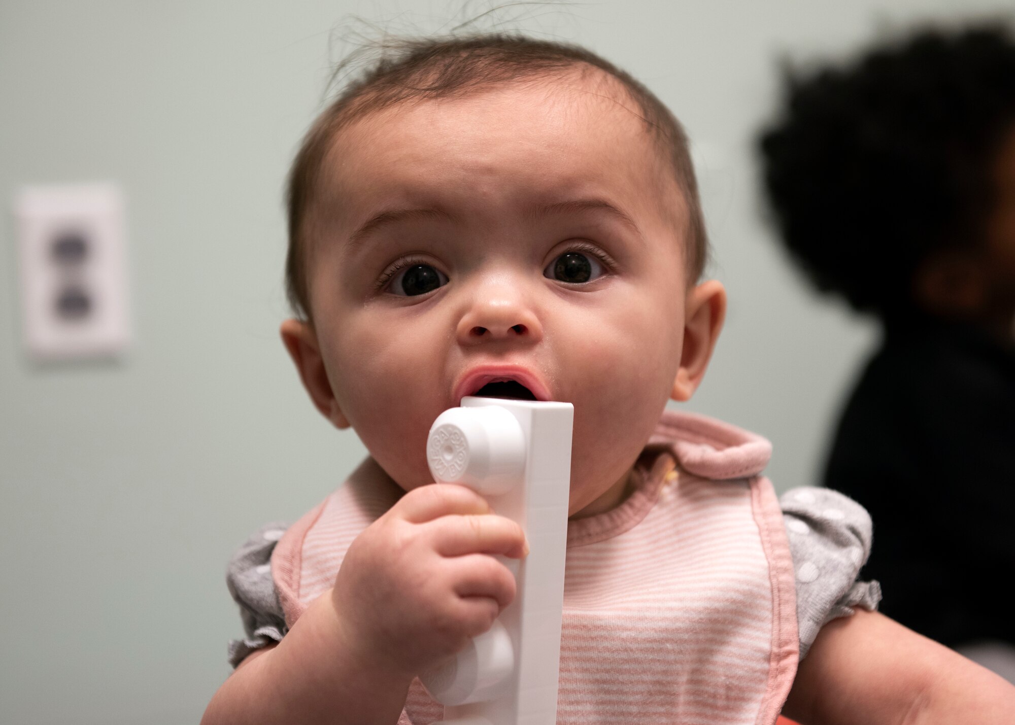 Photo of a baby holding a block in front of a wall in a room