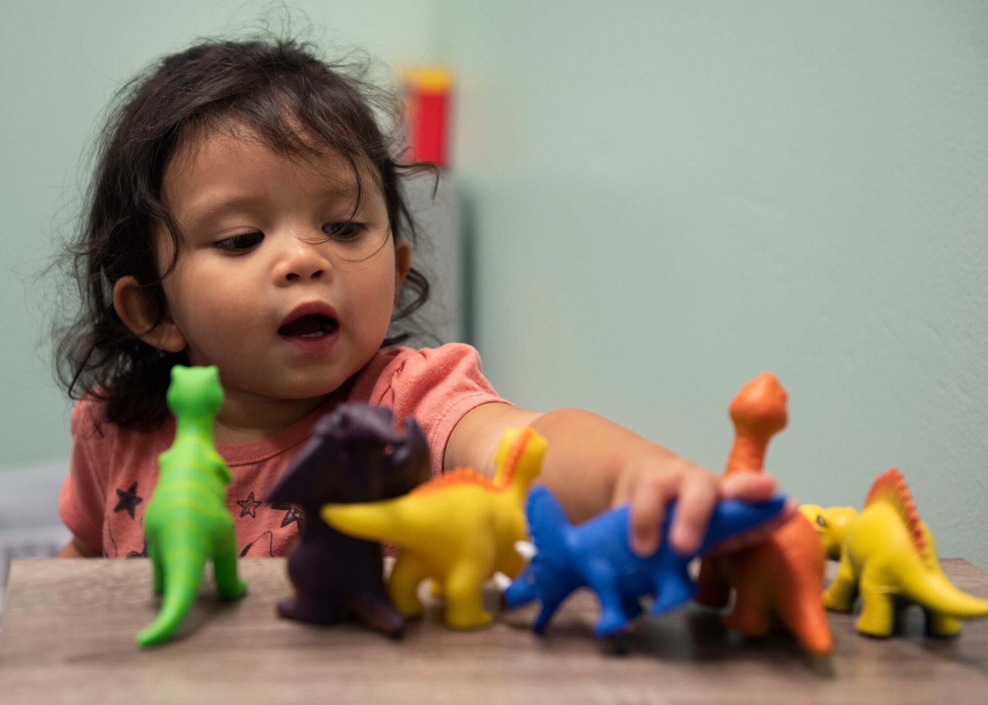 Photo of child playing with dinosaur toys on a table in a room.