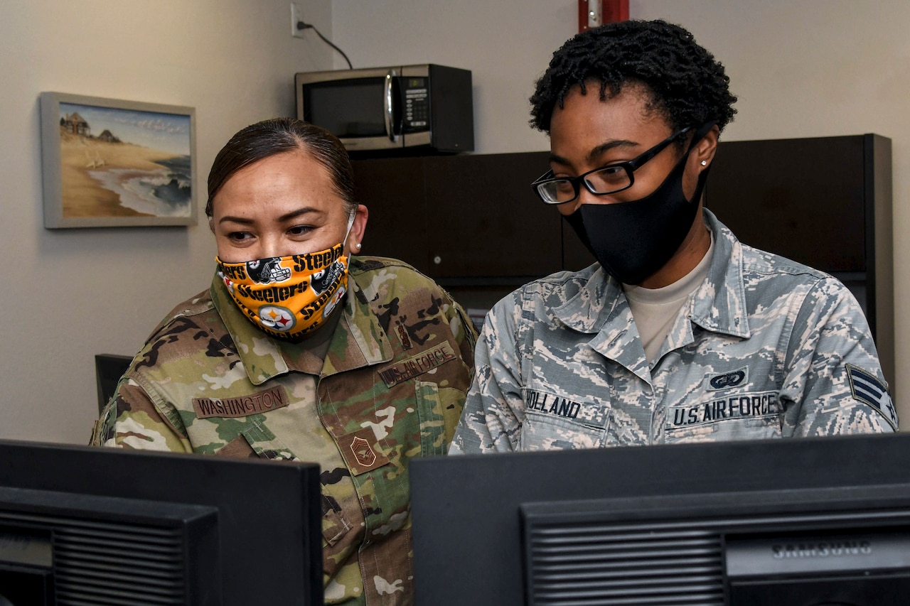 Two airmen look at computer screens.