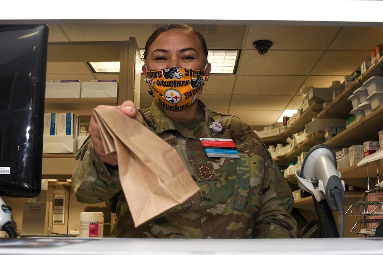 An airman wearing a mask holds out a brown paper bag from behind a counter.