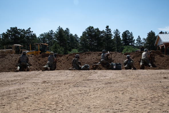 Six Airmen with rifles lined up behind a dirt mound, taking cover after hearing simulated gunfire in the distance during an exercise.