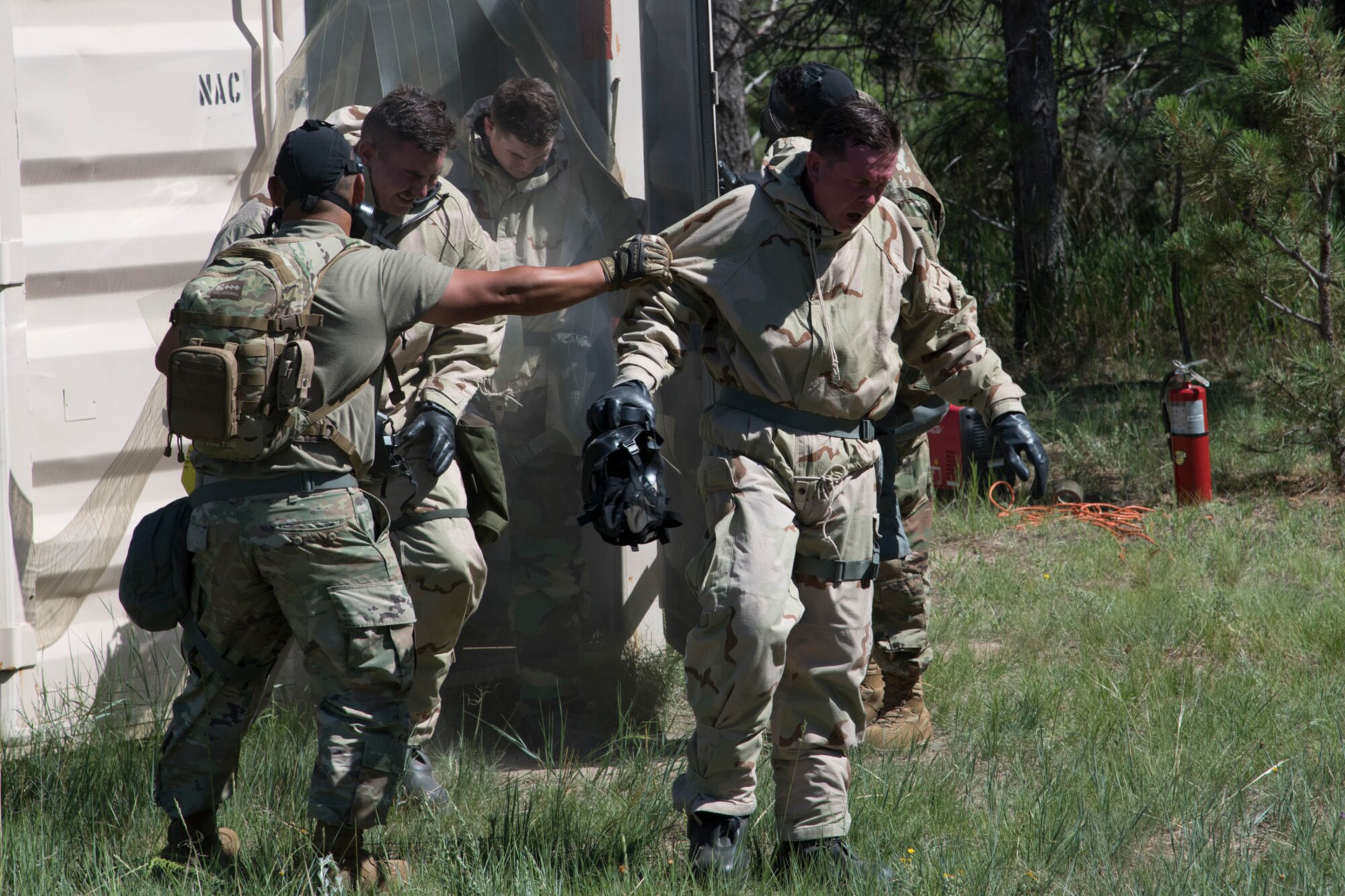 Airmen in chemical protective gear with their gas masks removed exit a connex container that was repurposed into a gas chamber.