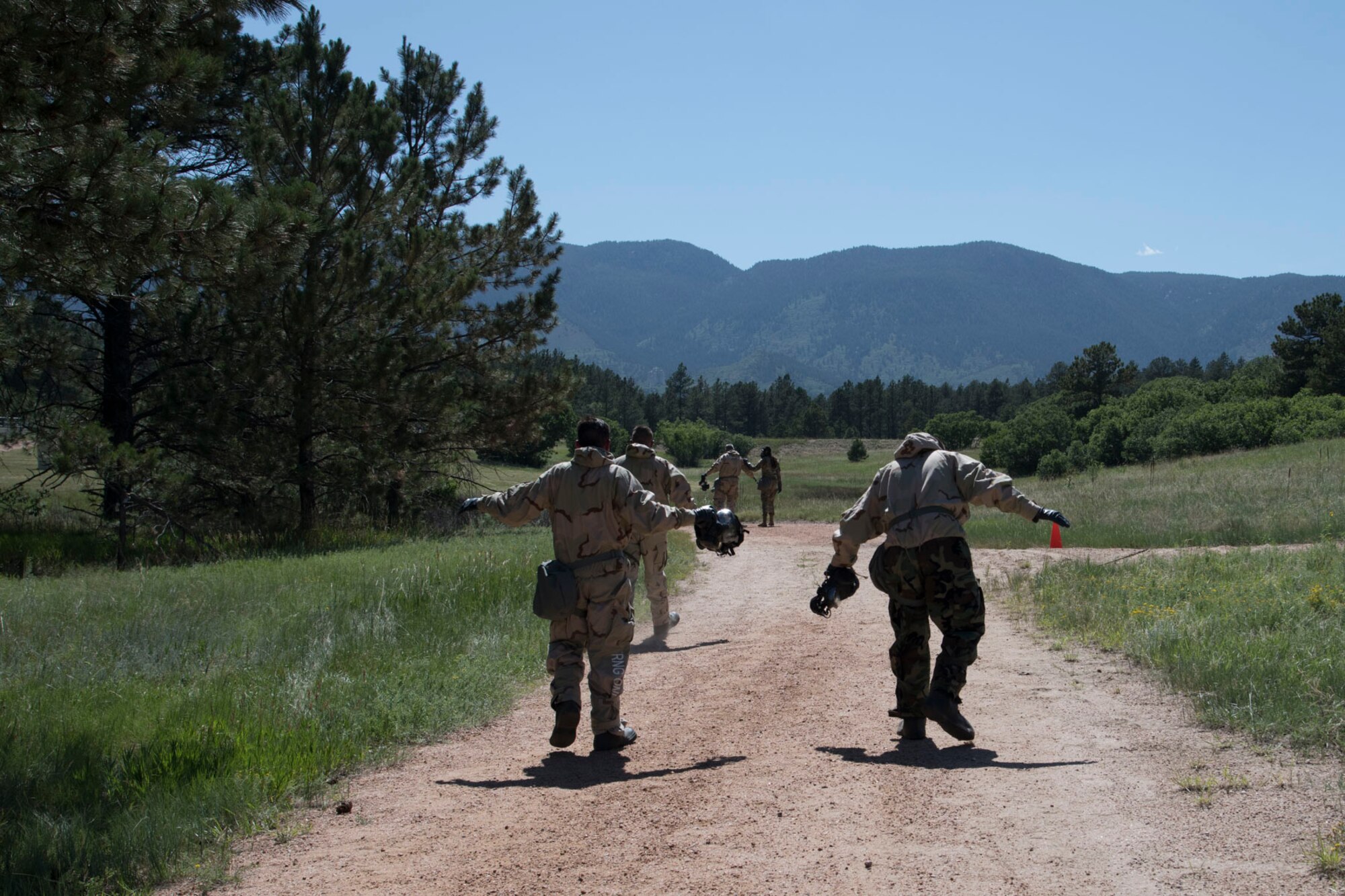 Airmen that just exited the gas chamber hold their arms out walking down a path with a mountain view horizon in the distance.