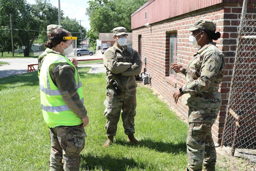 Three Nebraska National Guardsmen wearing face masks stand in grass.