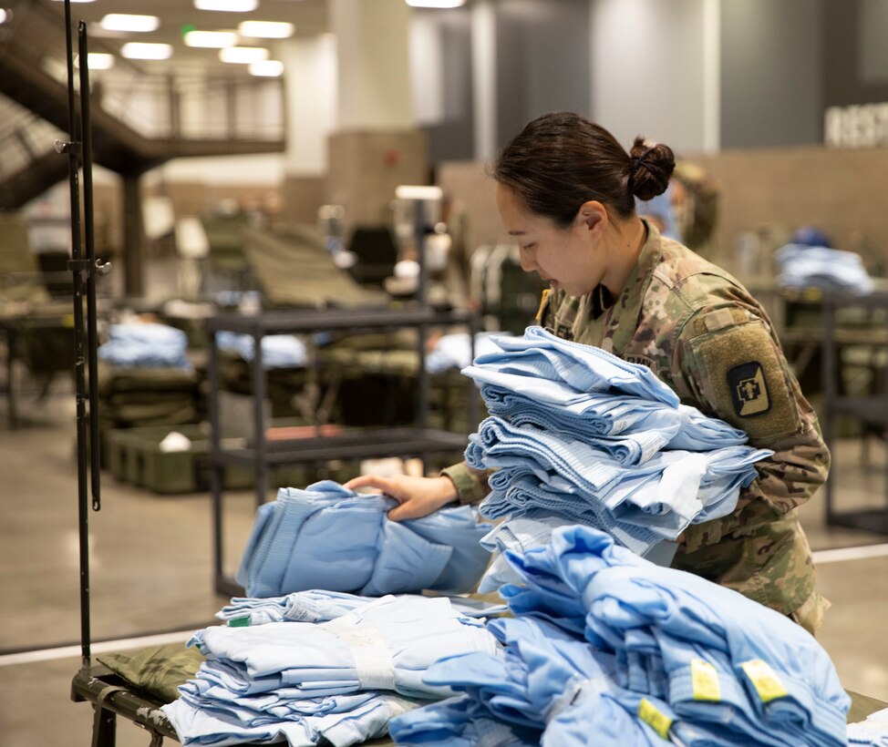 A soldier sorts through stacks of linens and hospital gowns on a table.