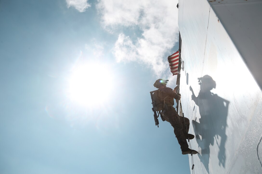 A Marine climbs a ladder in bright sunshine.