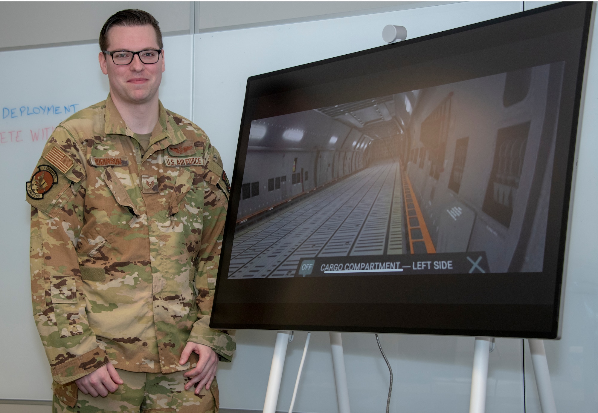 U.S. Air Force Staff Sgt. Kevin Robinson, 22nd Airlift Squadron evaluator loadmaster, stands near a monitor displaying virtual reality technology helps train aircrew July 21, 2020, at Travis Air Force Base, California. Robinson is the 60th Air Mobility Wing Warrior of the Week for June 14-20, 2020.  The program recognizes outstanding Airmen who have made significant contributions to their unit. (U.S. Air Force photo by Heide Couch