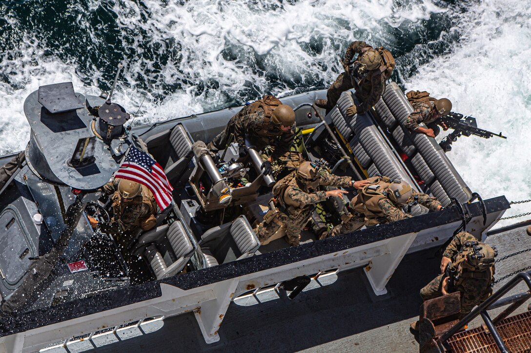 Marines rush to exit a boat in swirling waters.