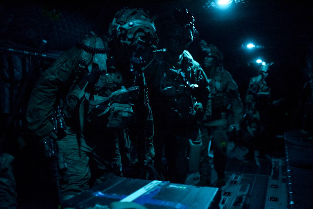 Soldiers gather in a dark helicopter illuminated by blue light.