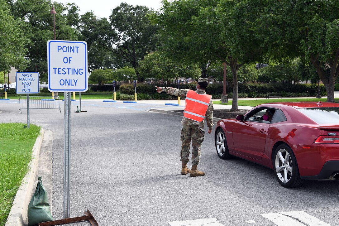 A soldier wearing a face mask assists a motorist at at COVID-19 test site.