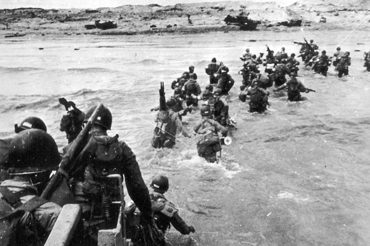 In a historic photo, a group of soldiers in combat gear wades through the hip-deep water as they head to a shoreline.