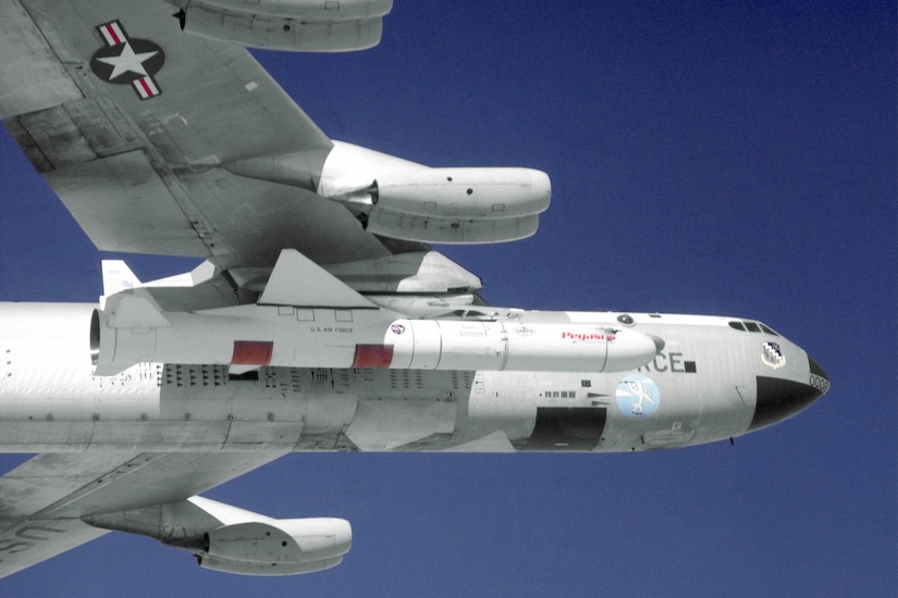 The underside of an aircraft is seen against a blue sky. A missile is attached to the underside of the wing.