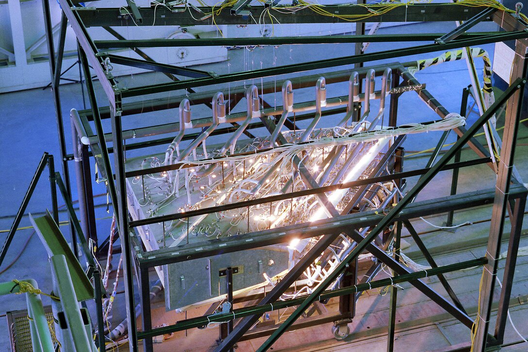 Coils and bright lights can be seen atop equipment that is inside a glass-paneled metal frame.