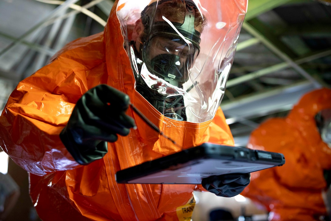 A soldier wearing a protective suit holds a plastic item.