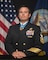 Posing for the picture in his uniform, wearing medal of honor with american flag and navy flag in the background