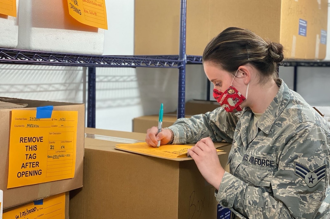 A guardsman wearing a mask checks a list of a shipment of personal protective equipment.