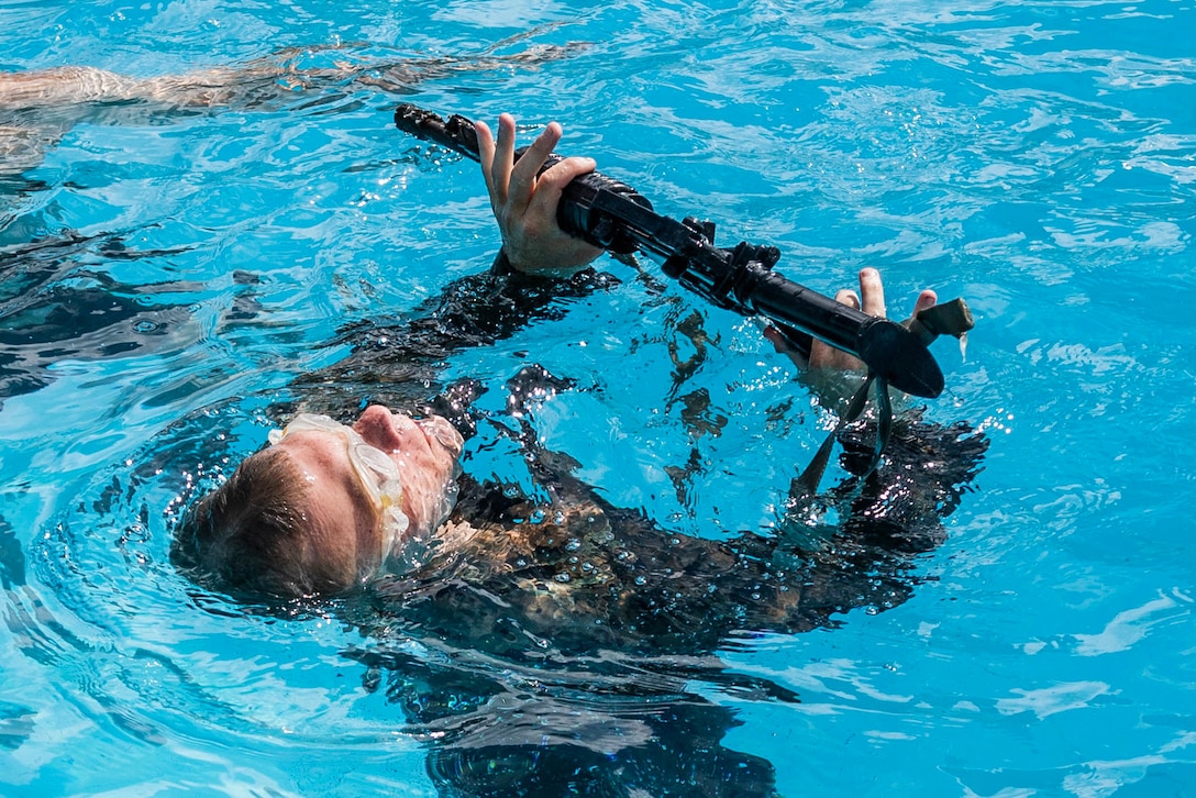 A Marine balances a rifle in a pool.